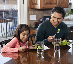 Hombre y niña comiendo una comida saludable en su casa.